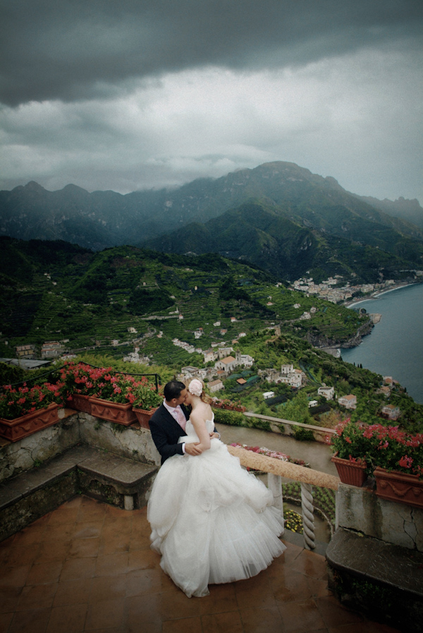 beautiful image of the bride and groom embracing on a balcony that overlooks a stunning landscape - bride is wearing a white ball gown style dress -  photo by Italian wedding photographer JoAnne Dunn